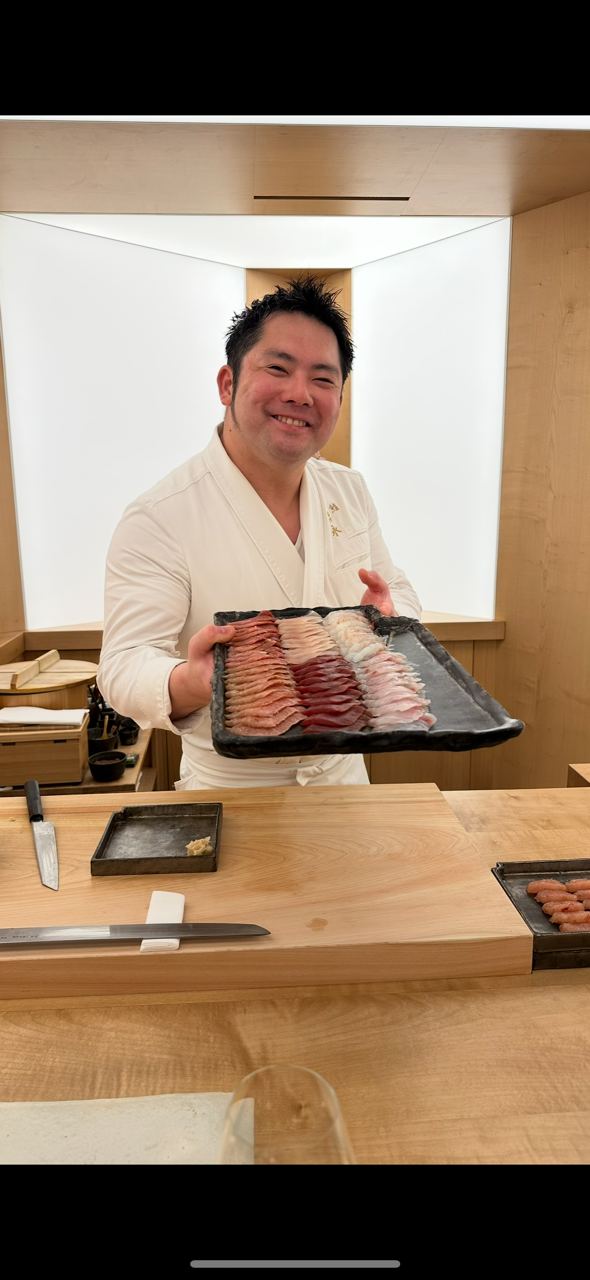 Conciergerie de luxe Paris, chef sushi présentant un plateau de poissons tranchés derrière son comptoir omakase